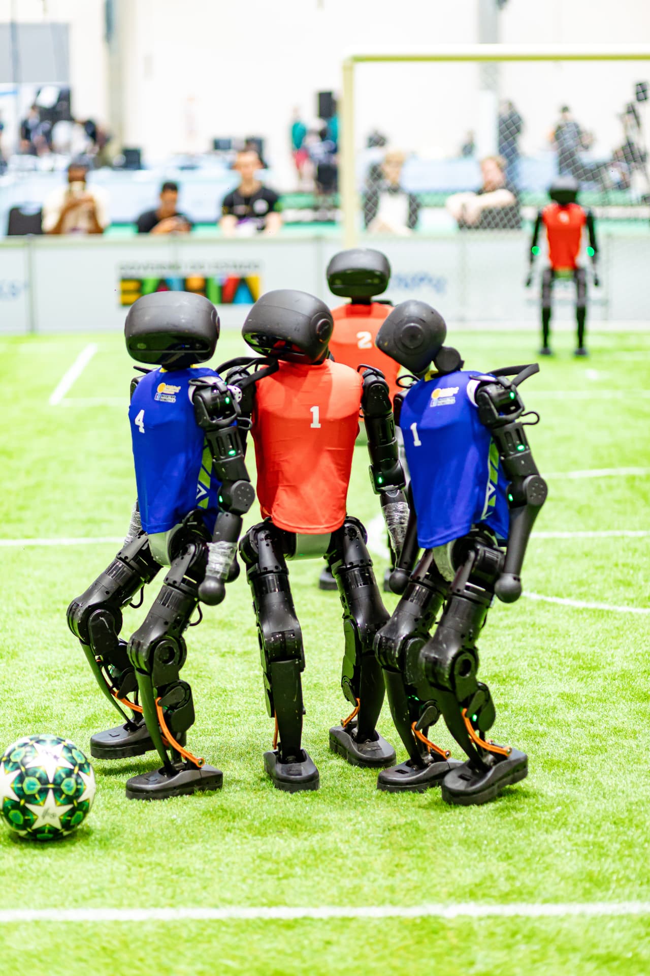 Quatro robôs com coletes azul e vermelho disputando a bola